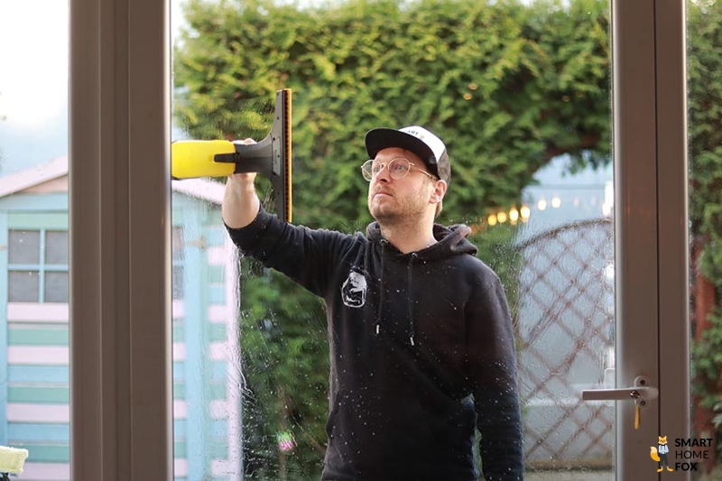 Man sieht wie ein Mann Fenster draußen reinigt mit dem Fenstersauger.
